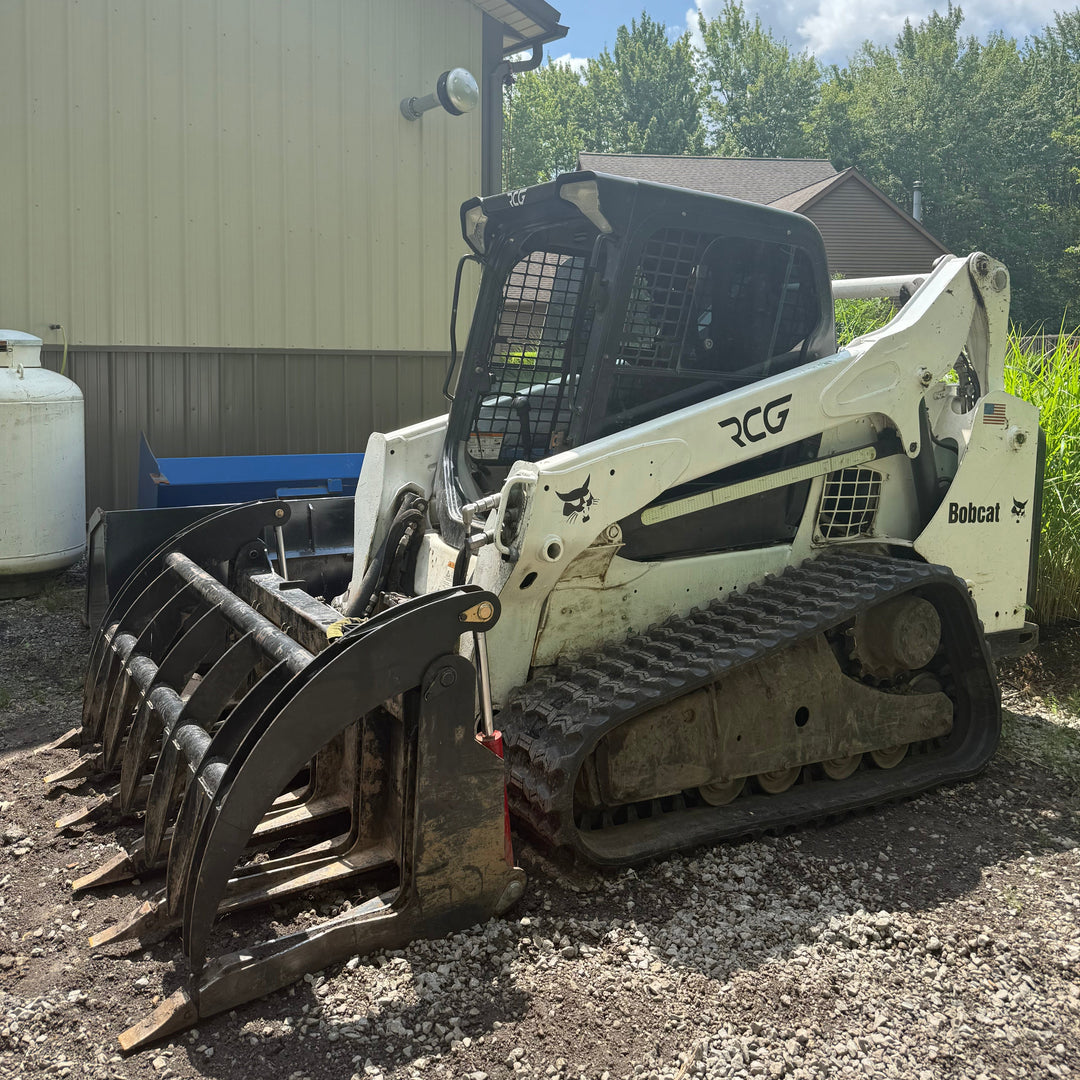 Bobcat track loader on a gravel surface with a building and trees in the background