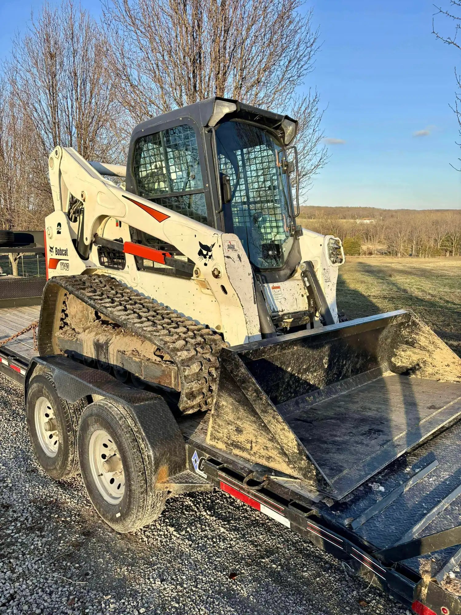 White Bobcat compact track loader with a front bucket, loaded on a utility trailer.