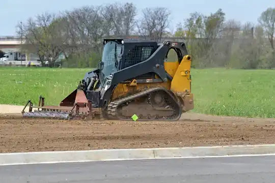 Yellow and black compact track loader with a soil conditioner attachment.