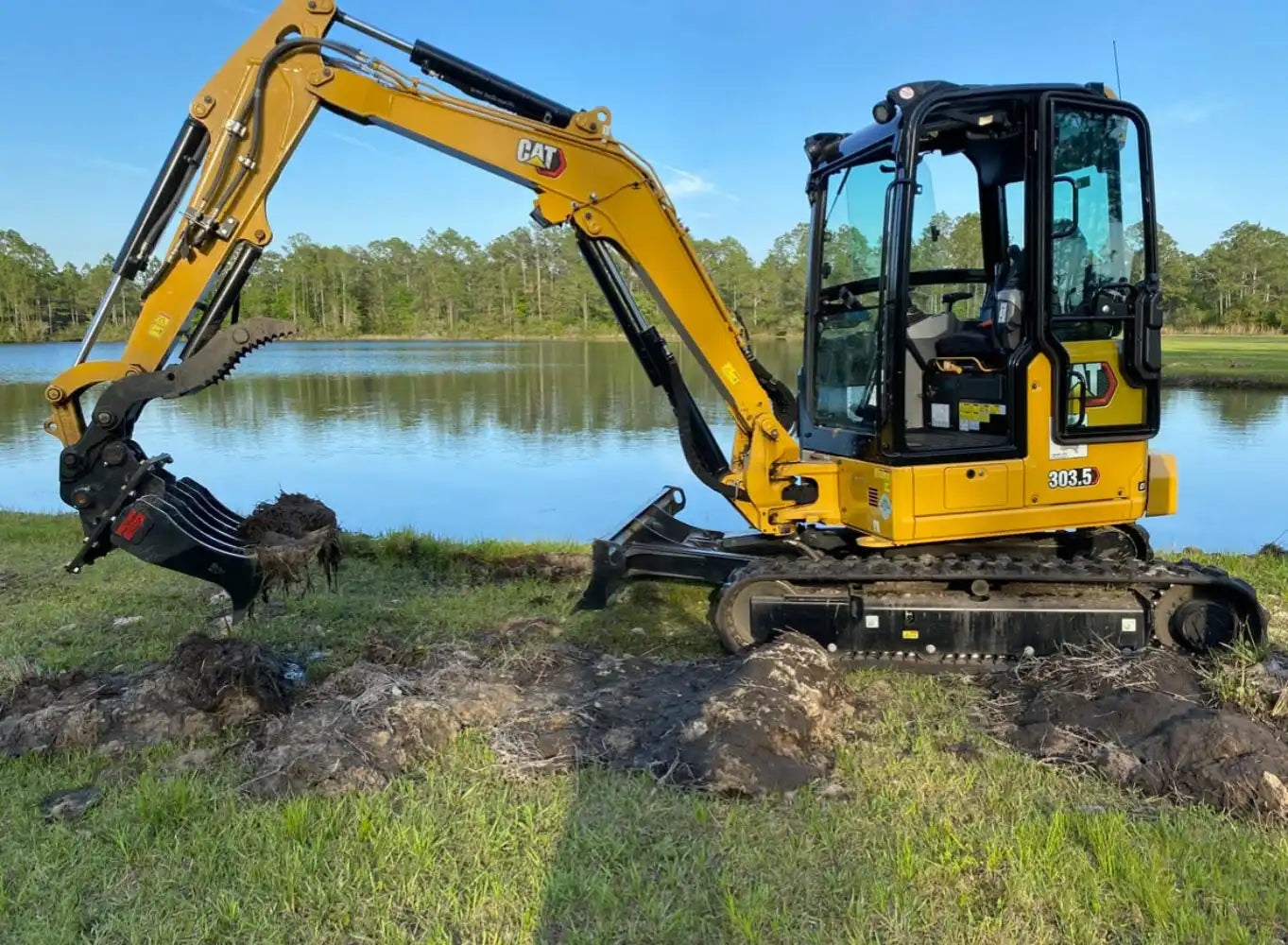 CAT 303.5 mini excavator with rubber tracks lifting soil on lakeside project